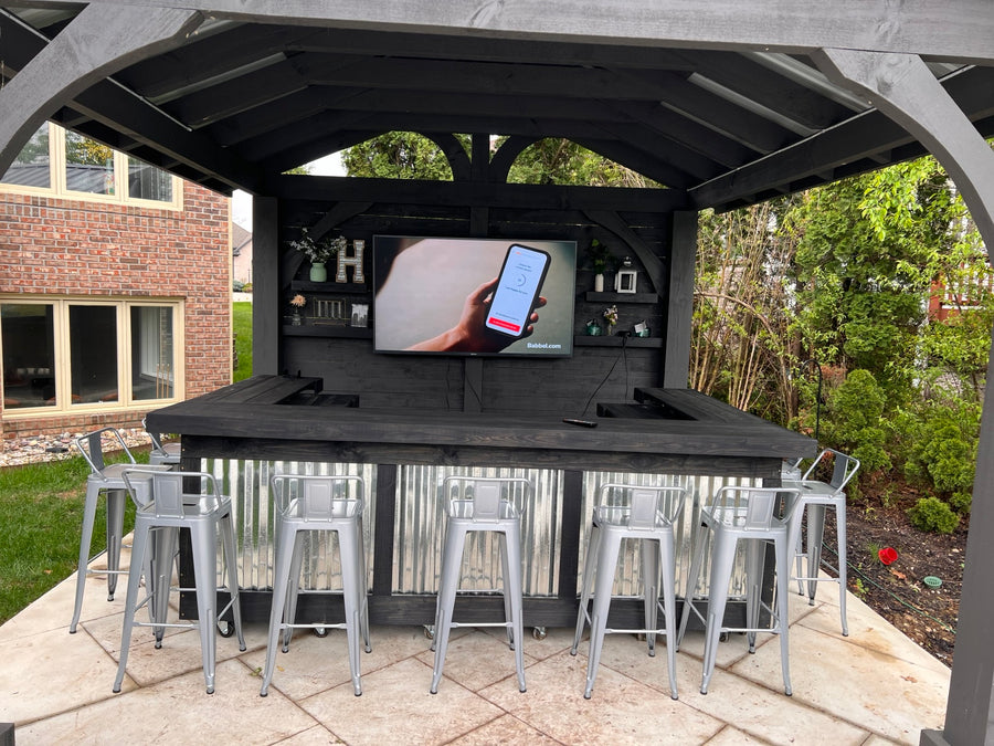 Black wood and corrugated metal U-shaped bar beneath a matching backyard gazebo