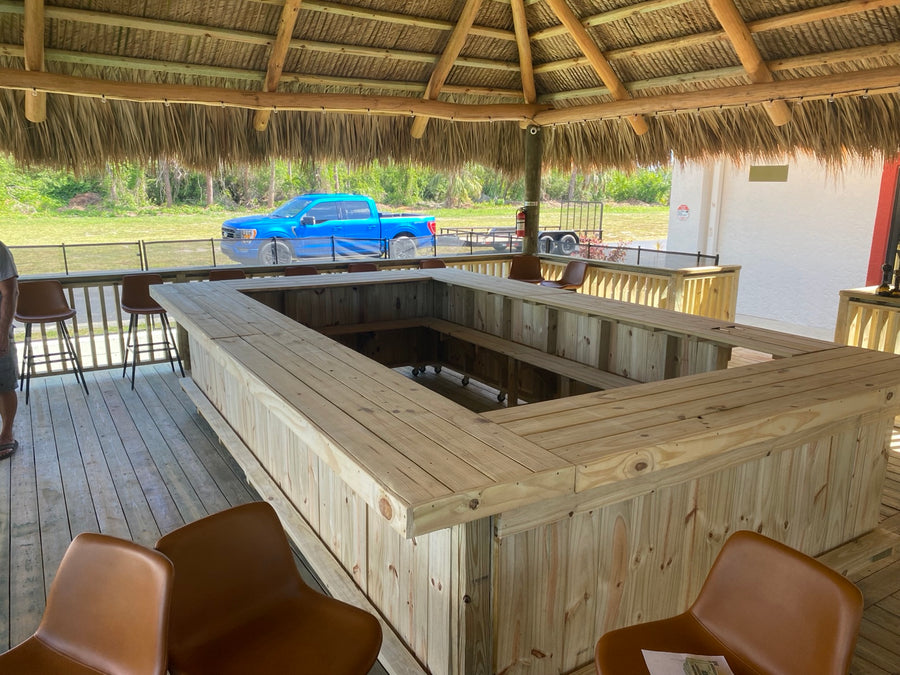 Large natural wood U-shaped bar with stools beneath a thatched roof