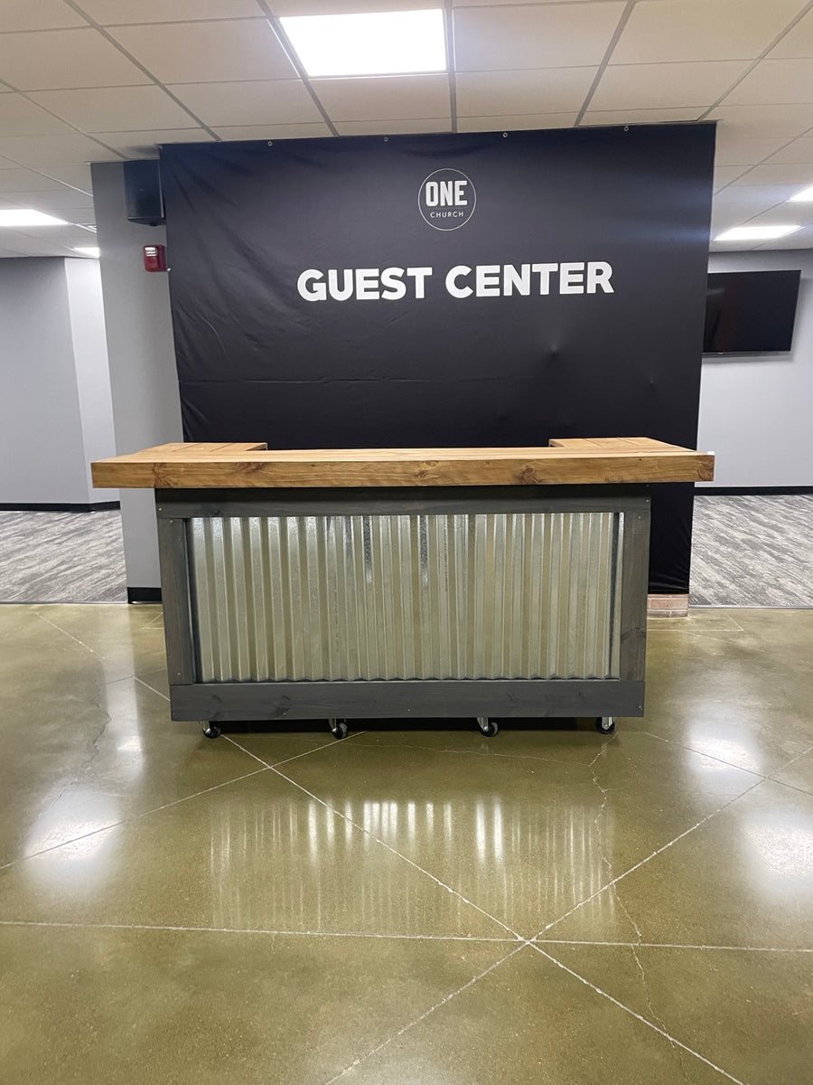 Wood-topped reception counter with a dark frame and corrugated metal front at a church guest center