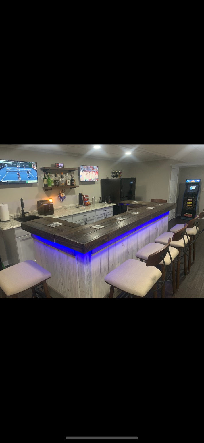 White wood U-shaped bar with a dark top and blue accent lighting in a basement