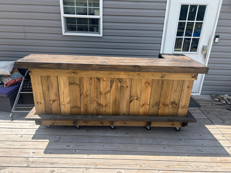 Natural wood straight bar with a dark countertop and foot rail on a deck