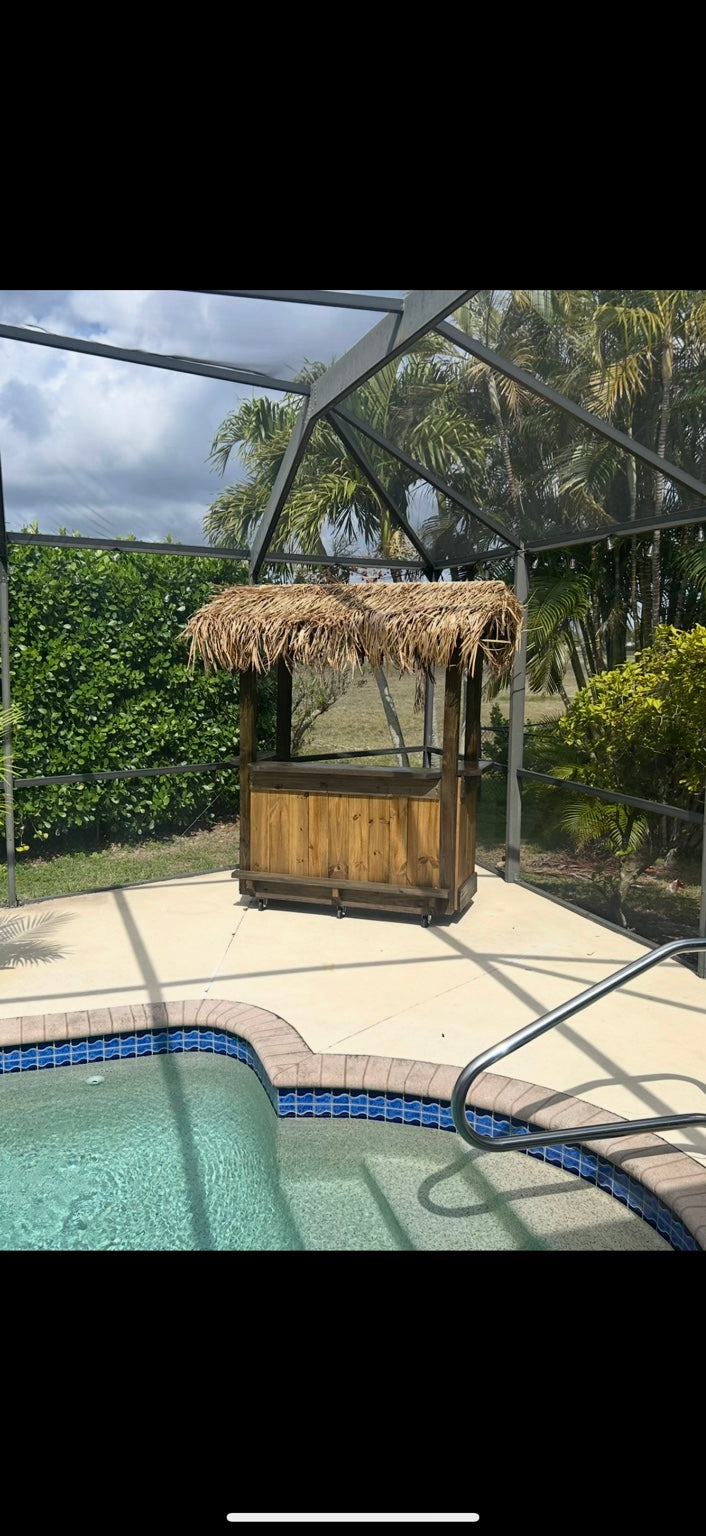 Compact wood tiki bar with a thatched roof beside a screened-in swimming pool