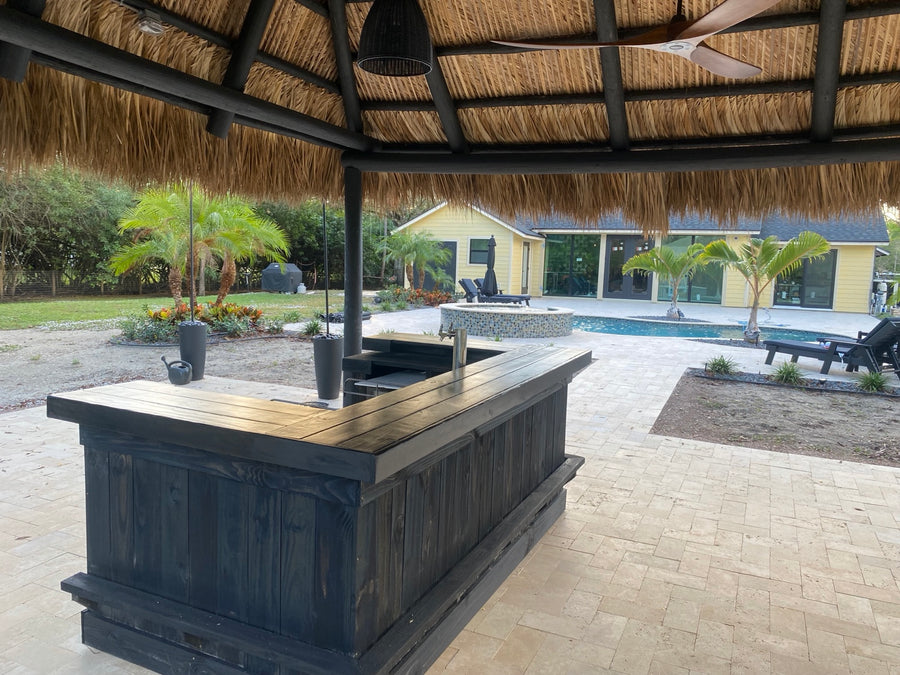 Dark wood L-shaped bar beneath a thatched shelter on a paved patio