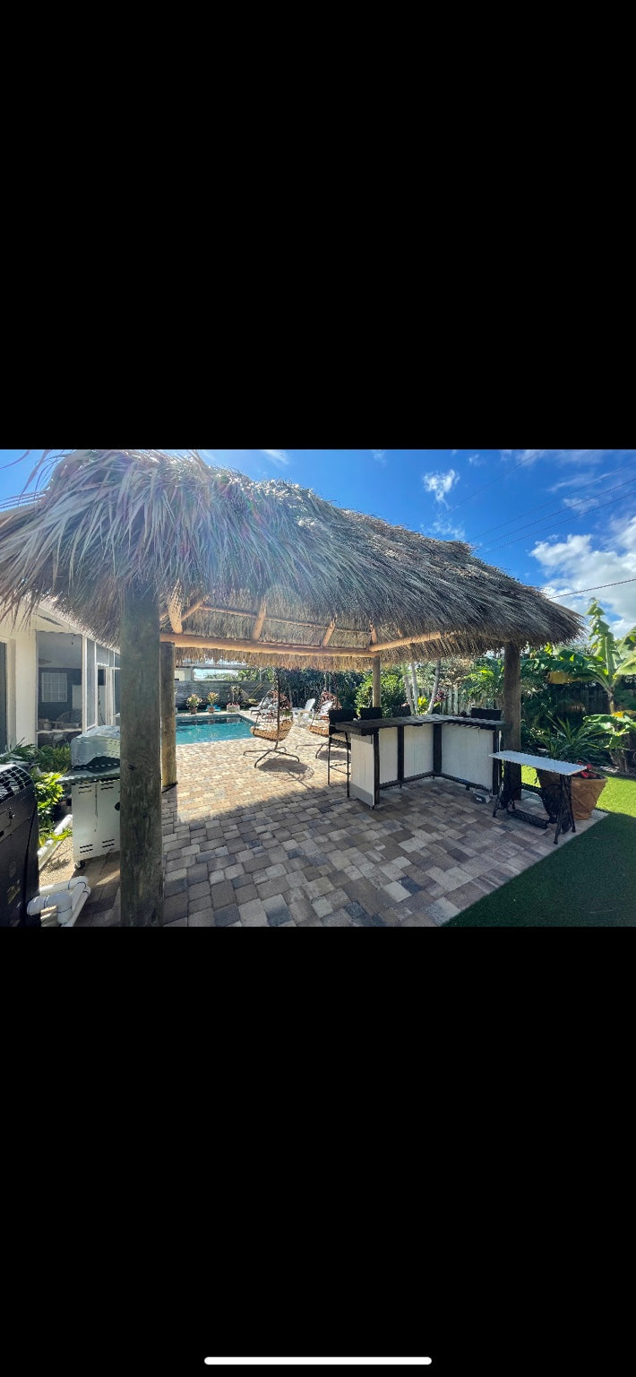 White-paneled L-shaped bar beneath a thatched shelter near a backyard swimming pool
