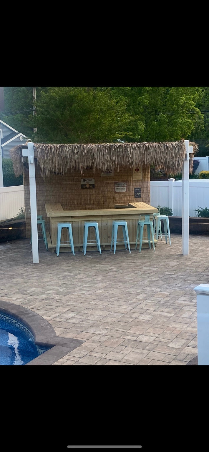 Wood bar with a thatched roof and stools beside a swimming pool